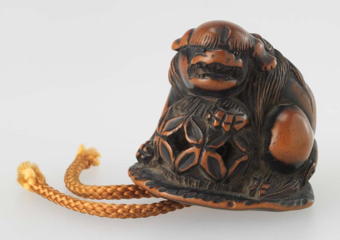 Artwork Netsuke:  (shishi (lion) with magic) this artwork made of Carved boxwood with yellow cord, created in 1830-01-01