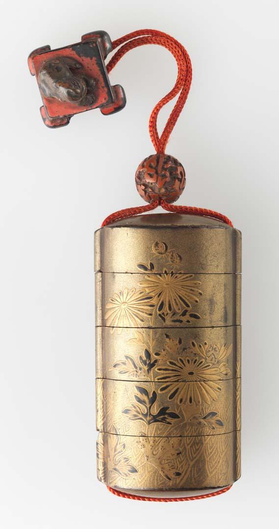 Artwork Inro with netsuke:  (chrysanthemum motif) this artwork made of Wood with black lacquer and gold leaf.  Lacquer toggle and netsuke of a lion on a table with red cord, created in 1800-01-01