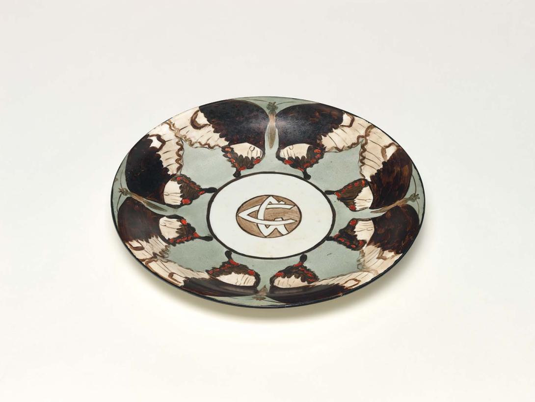 Artwork Plate this artwork made of China painted white earthenware with border of four butterflies in black/brown, white and red against a grey ground enclosing GC (in monogram) black rim, created in 1915-01-01