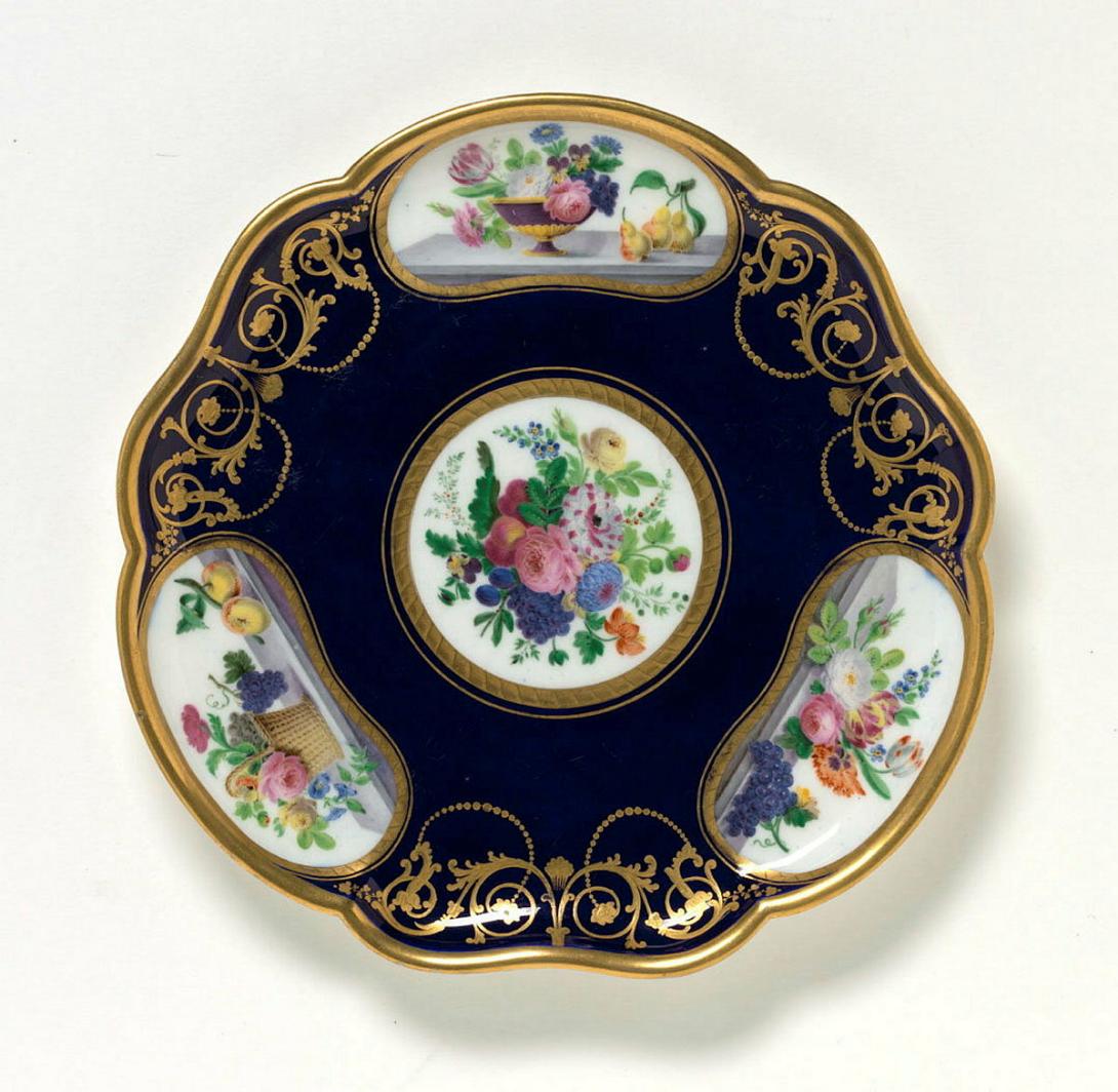 Artwork Plate this artwork made of Soft-paste porcelain, lobed trefoil shape in bleu roi ground reserving a central circular shape and three kidney shapes painted with floral bunches.  Gilt scrolls, created in 1764-01-01