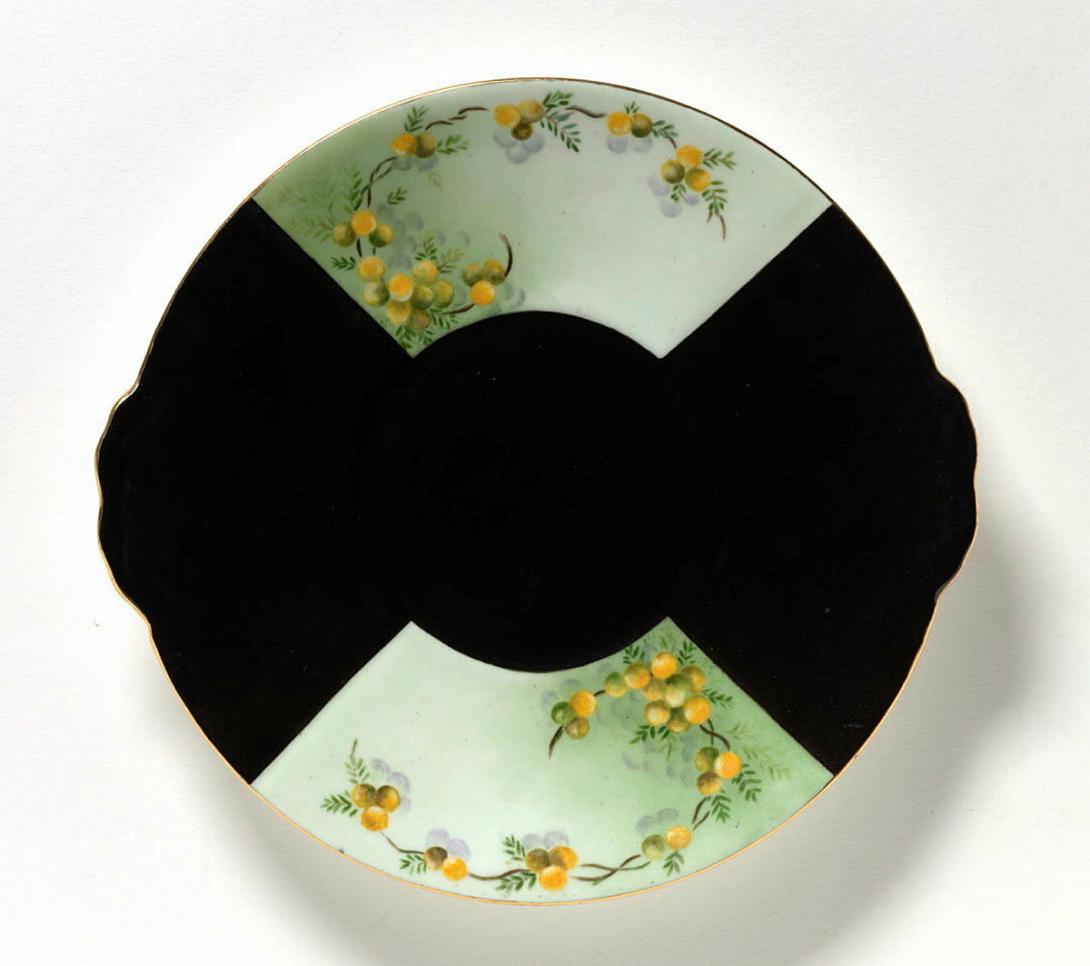 Artwork Plate:  Wattle this artwork made of Porcelain blank painted black with fan shaped reserves painted in green, brown, yellow and mauve overglaze colours and gilt, created in 1955-01-01