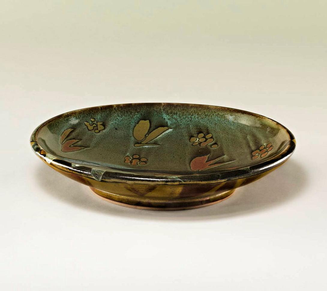 Artwork Dish with landscape decoration this artwork made of Stoneware, wheelthrown with iron oxide glaze and poured limestone and trailed celadon glazes over wax resist