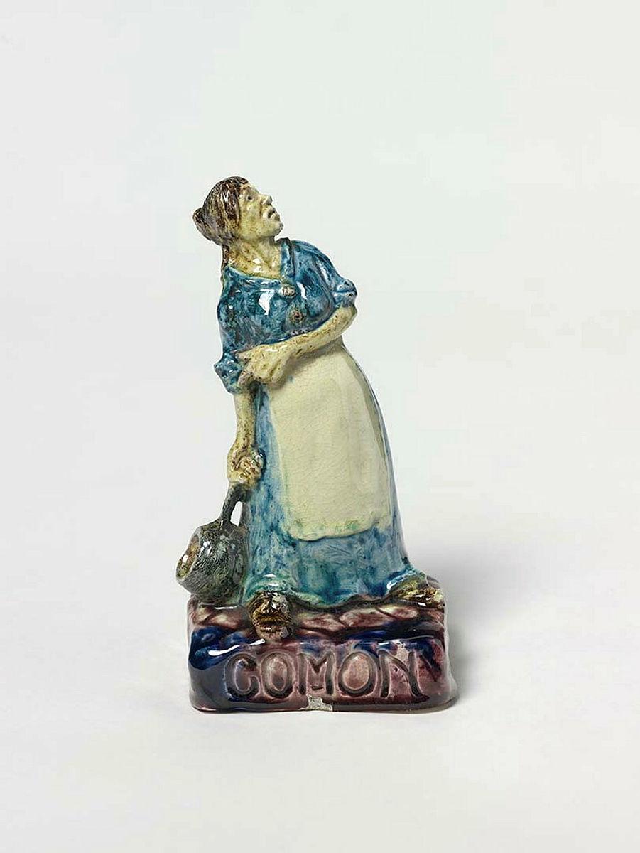 Artwork Figurine: Comon this artwork made of Earthenware, press-moulded clay in the figure of a pioneer woman with a saucepan on a rusticated base. Glaze picked out in mulberry and blue/green, created in 1930-01-01