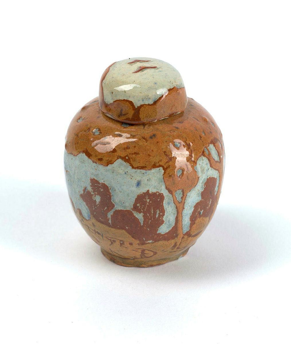 Artwork Small covered jar: Bush scene with shed this artwork made of Earthenware, gold and terracotta clays over white, incised with a bush scene with shed and fence. Light blue glaze, created in 1925-01-01