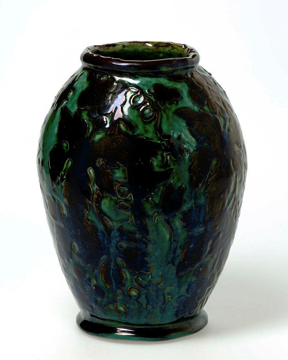 Artwork Vase this artwork made of Earthenware, hand-built white clay dipped brown and carved with a design of grape leaves, fruit, tendrils and insects.  Glazed blue/green, created in 1927-01-01
