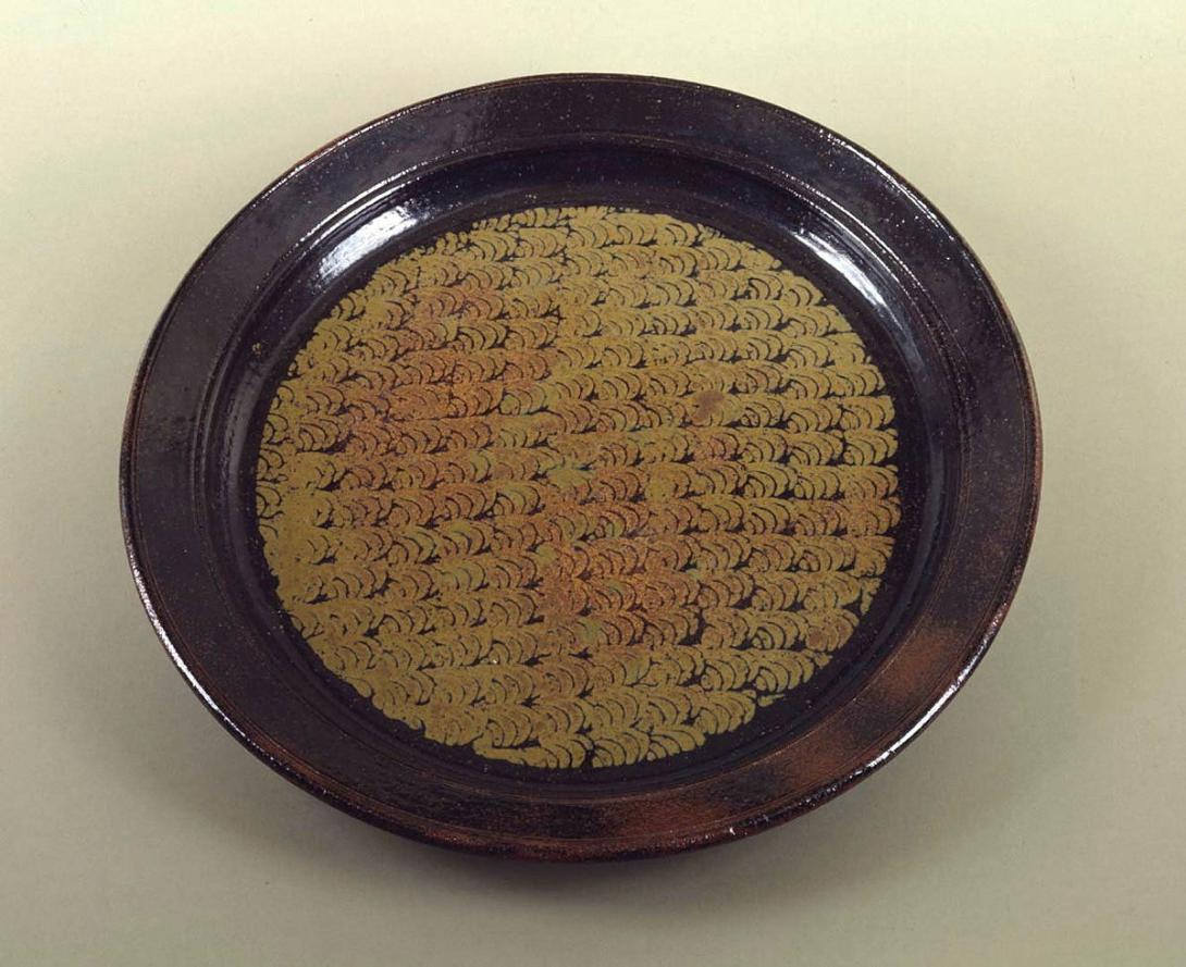 Artwork Platter this artwork made of Stoneware, thrown with tenmoku glaze with motif stamped in rutile, reduction fired to 1280 degrees Celsius in a fibre kiln with LP gas, created in 1980-01-01