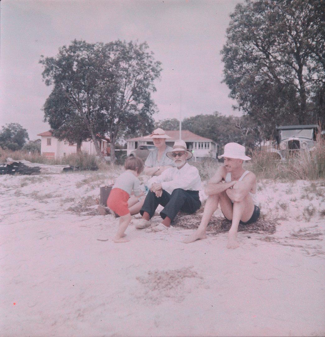 Artwork (Family on shore, houses in background, l.r.:  unidentified small girl, Marjory Simmonds, J.H. Simmonds, Snr, J.H. Simmonds, Jnr) this artwork made of Cellulose acetate Dufay colour transparency (originally in a glass mount), created in 1935-01-01