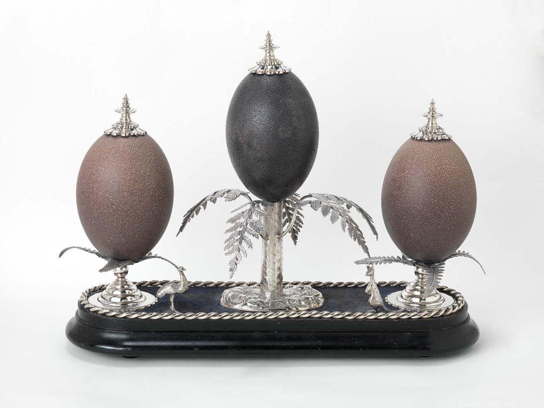Artwork Table decoration this artwork made of Silver, emu eggs mounted on silver tree ferns on a blue velvet and ebonised wood base. Silver and rope edge and cast figures of a kangaroo and emu, created in 1860-01-01