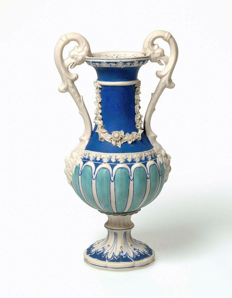 Artwork Handled vase this artwork made of Porcelain (parian) of swelling section with snake handles terminating in grotesque masks and swags of modelled flowers around the neck. Painted, blue turquoise and yellow
