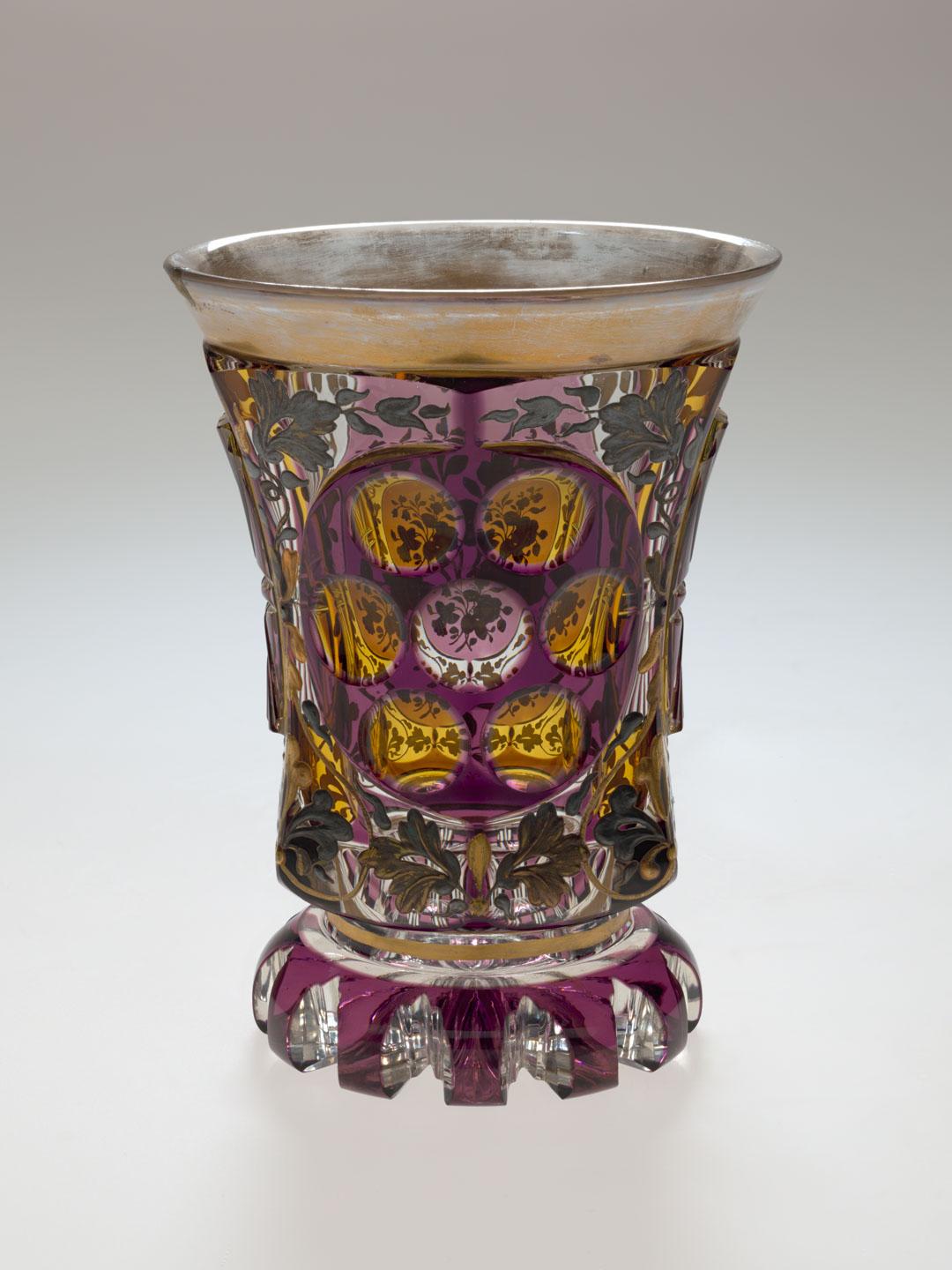 Artwork Beaker this artwork made of Glass, cased amethyst over clear and cut away in panels stained yellow.  Applied with gilt and gunmetal floral motifs, created in 1840-01-01