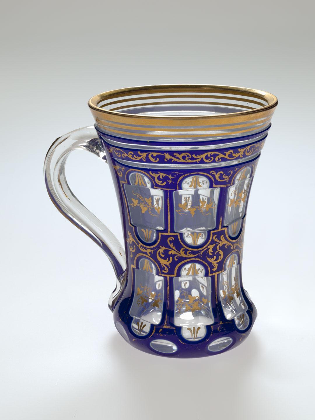 Artwork Beaker with handle this artwork made of Opaque royal blue glass cased over clear and wheelcut in panels and with gilt ivy leaf decoration, created in 1840-01-01