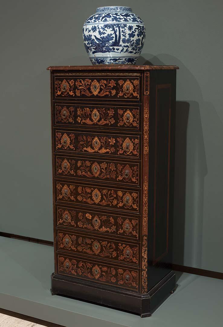 Artwork Wellington chest this artwork made of Ebonised wood, the eight drawers inlaid in various woods with scrolls, flowers and cartouches framing the bronze key escutcheons and lion mask handles. Brown marble top, created in 1700-01-01