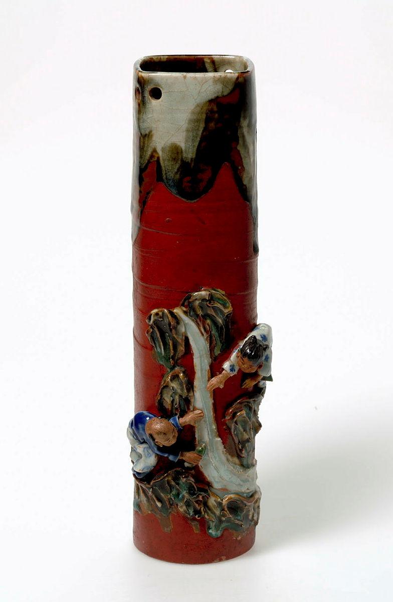 Artwork Wall vase this artwork made of Stoneware, thrown tall cylindrical shape, decorated and applied with modelled figures.  Glazed matt red, and colours, created in 1900-01-01
