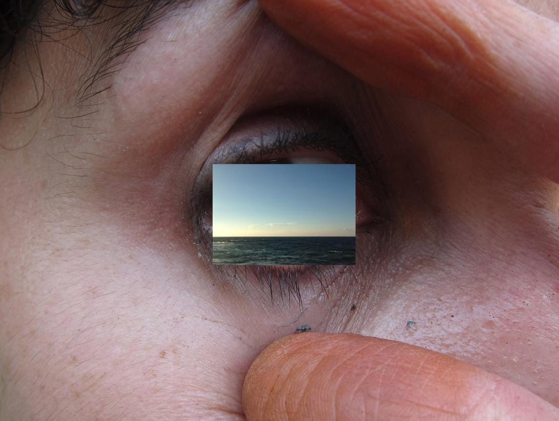 A close-up photograph of an eye, with the lids held open by someone's fingers. In place of the eye itself is an embedded photograph of the horizon line over the ocean.