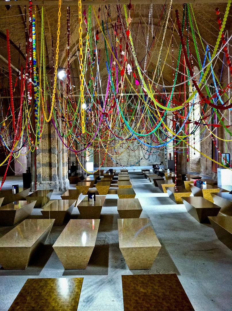 A photo of an installation with colourful beaded strands suspended over a room with benches.