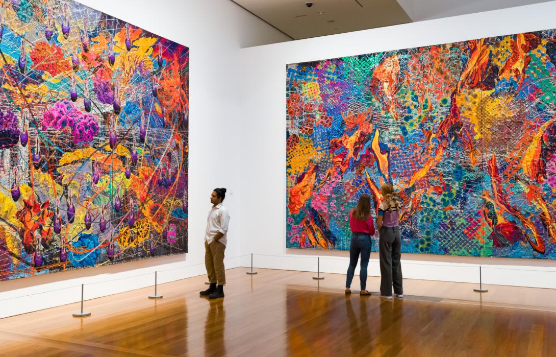 Three gallery visitors look upon two of three huge, colourful works by Thasnai Sethaseree.