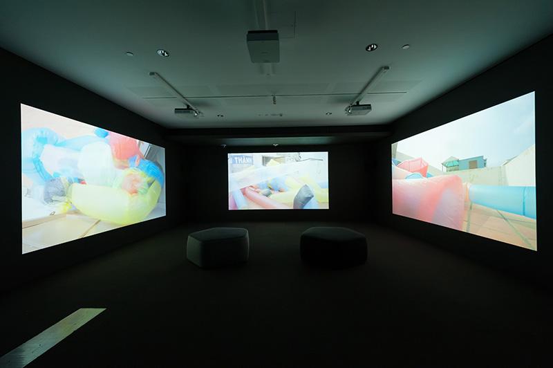 An installation view of a video work appearing across three walls of a dark room.