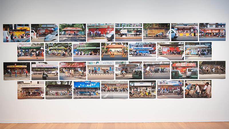 An installation view of four rows of printed photographs attached to a gallery wall.