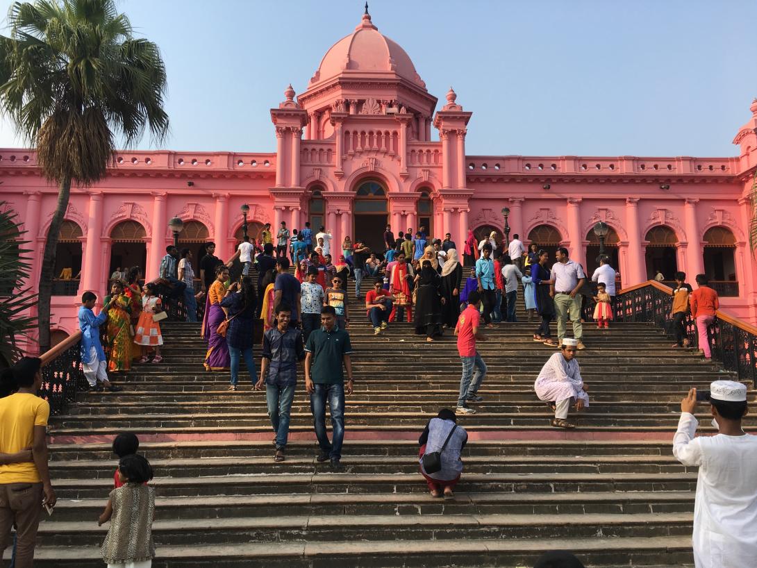 A photograph of crowds outside Ahsan Manzil, a bright pink palace.