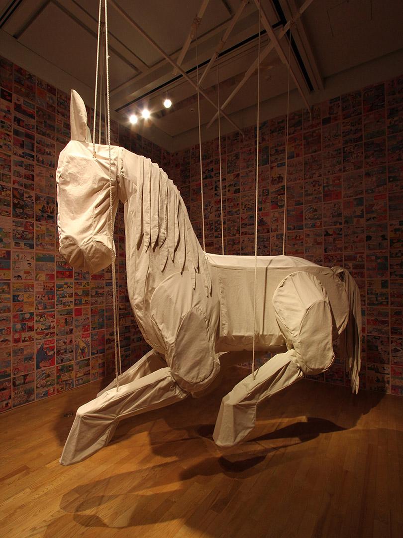 An installation view of a larger-than-life-size horse sculpture made of linen, suspended from the ceiling.