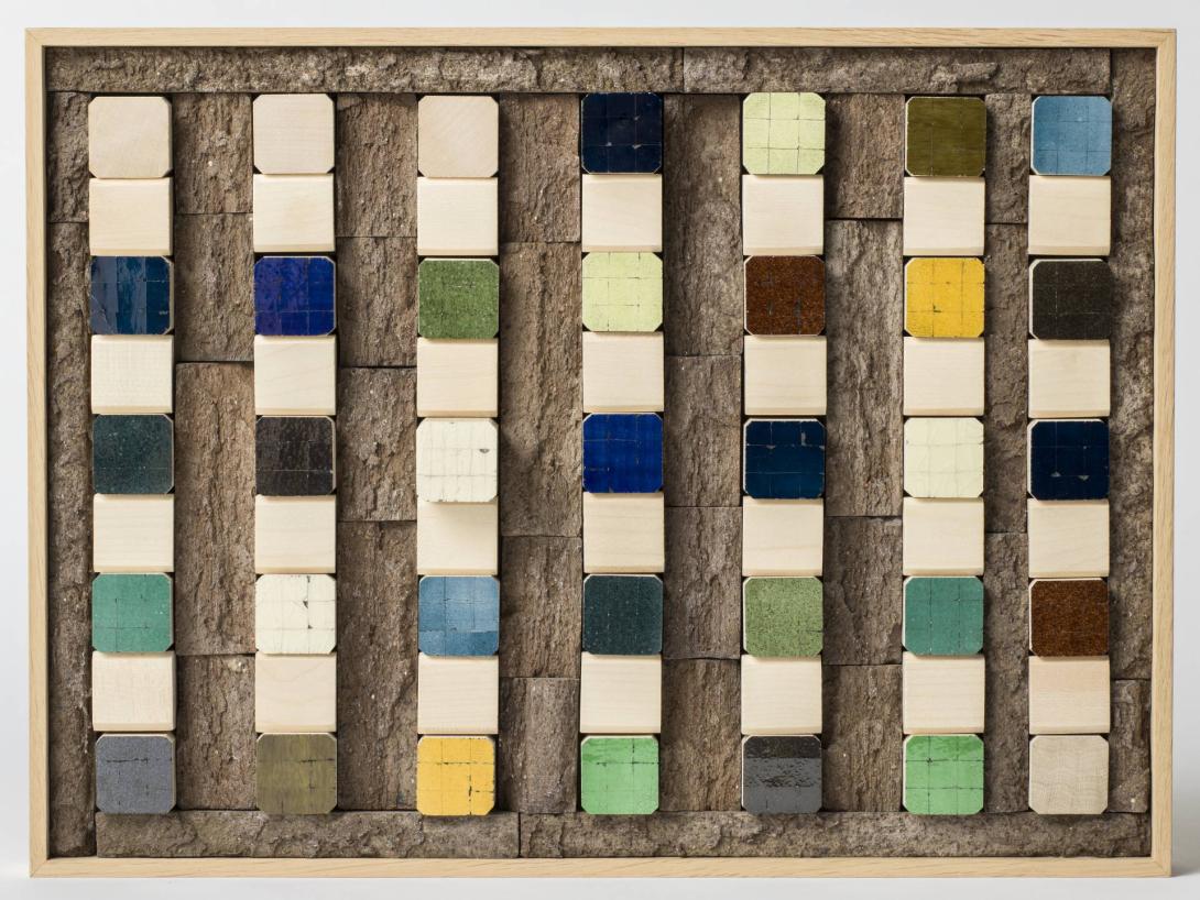 A sculptural work appearing to be a wooden board inset with eight columns of tiles in white, blue, black, green and yellow.