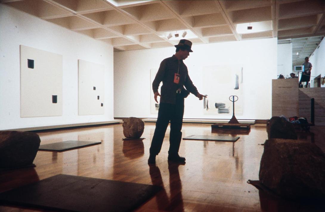 A photograph of an artist installing his work, which includes what look like large rocks, in a brightly lit gallery space.