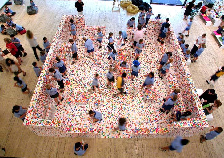 An installation view, photographed from above, of young visitors participating in stickering artist Yayoi Kusama's interactive work The Obliteration Room.