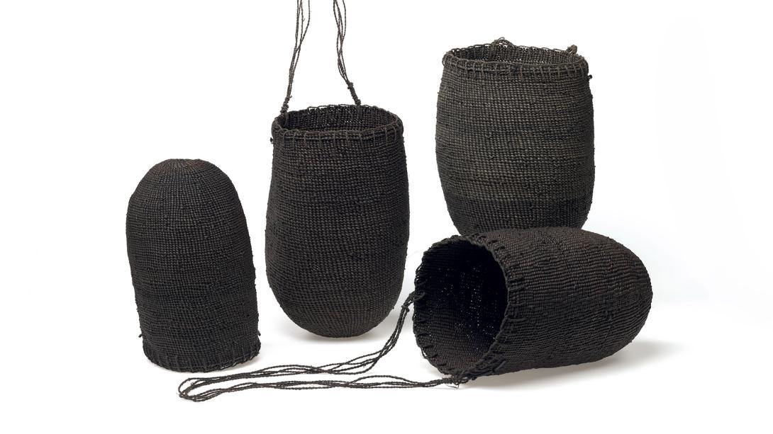 An installation view of four bags or baskets, woven from a dark fibre.
