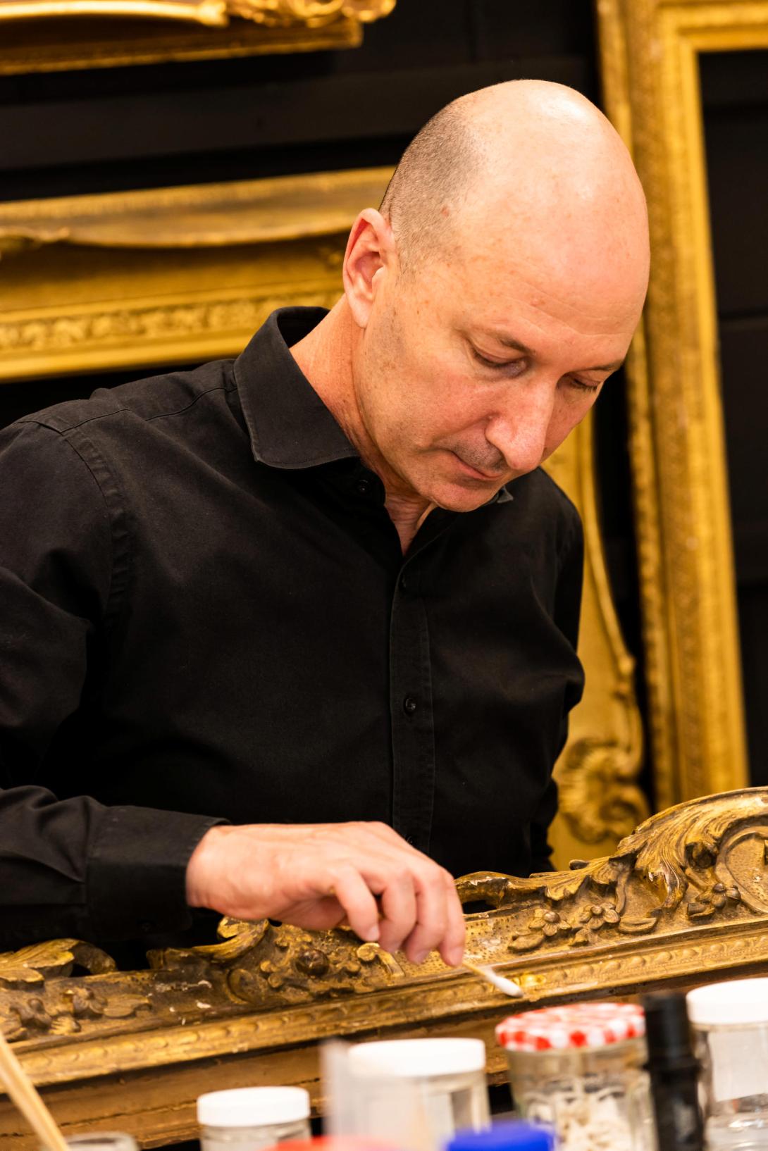 A man in a black shirt works on a gold-gilded frame in the QAG Framing Workshop.