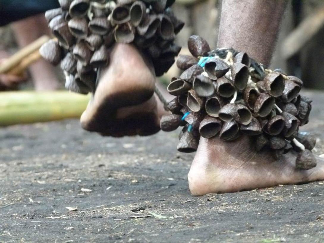 A close-up photograph of the bare feet of a dancing person; the person has anklets of seedpods that would jangle while dancing.