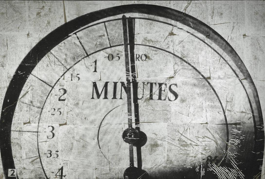 A black-and-white image of a clock, on which the numbers count backwards. Numbers are missing from the right-hand side of the clock. The hands point to 12:00 exactly.
