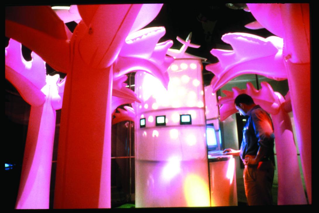 An installation view of an immersive artwork in which a visitor walks amongst inflatable neon pink trees. The photograph, taken in 1999, is grainy.